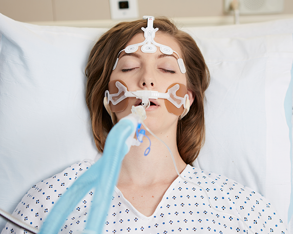 Intubated patient sleeping wearing hospital gown monitored by Masimo forehead sensor