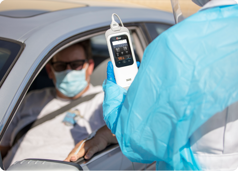 Clinician uses a Masimo Rad-G with Temperature device to check a masked patient’s vitals during drive-through screening.
